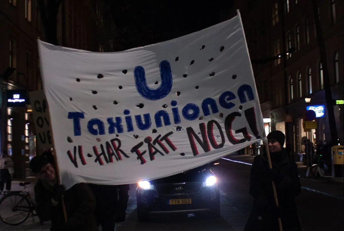 Demonstranter håller upp en banderoll med texten Taxiunionen – Vi har fått nog! på en gata i vinterkväll.