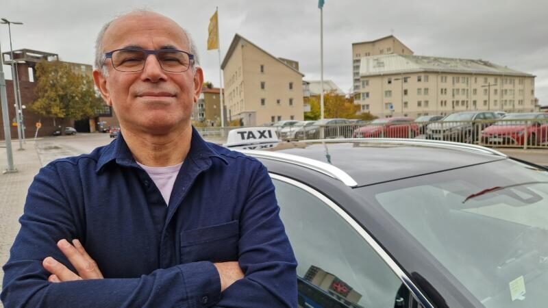 Taxiförare med korsade armar står vid sin bil med taxiskylt på taket.