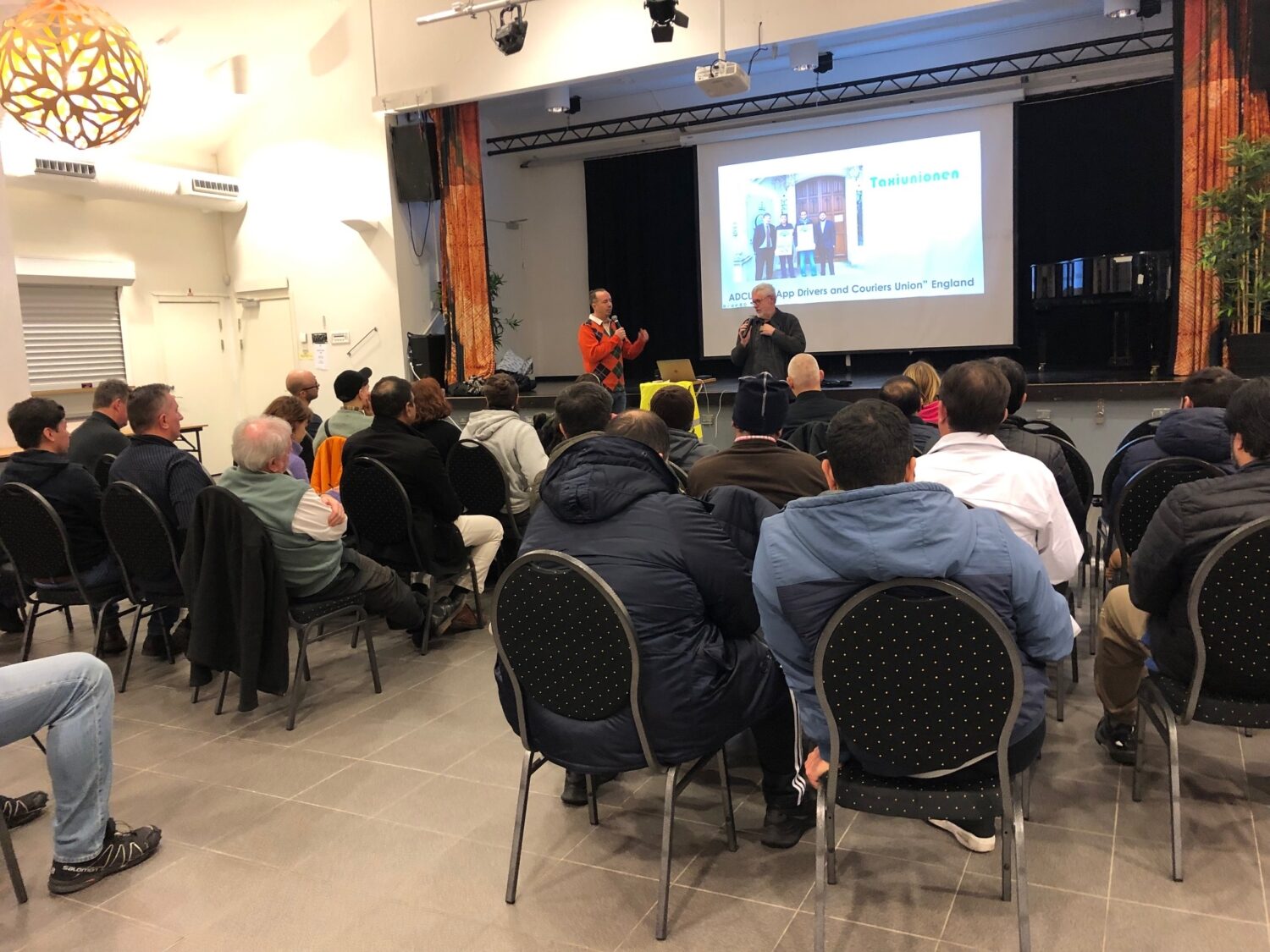 Fullsatt medlemsmöte i Folkets Husby i Järva, där förare lyssnar på en presentation om organisering.